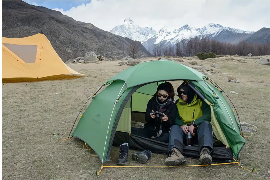 The tent is located in an open area with snow-capped mountains in the background, indicating that this tent is suitable for a variety of terrains.