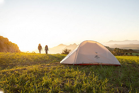 A photo taken at sunset shows two people standing in front of a tent.