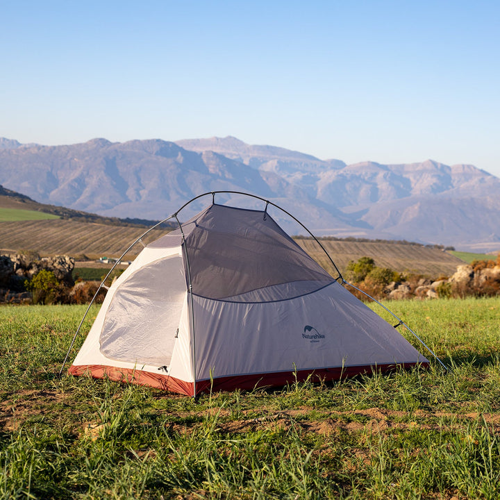 A tent is located on the grass. Surrounding the tent are some mountains and fields. The whole scene gives people a sense of tranquility and nature.