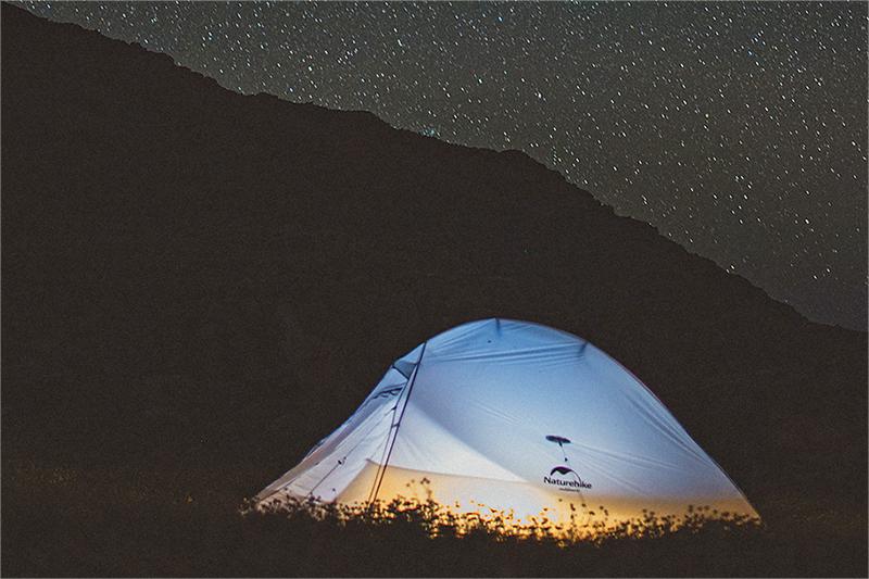 There is a white tent with the "Naturehike" brand logo under the starry sky. The whole scene looks peaceful and natural.